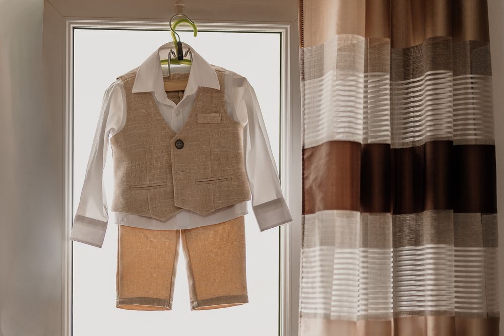Boys formal outfit with beige vest, white shirt, and tan shorts on a hanger against a light background.