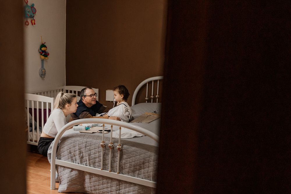 Family gathered around a child's bed in a cozy nursery room, sharing a warm bedtime moment together.