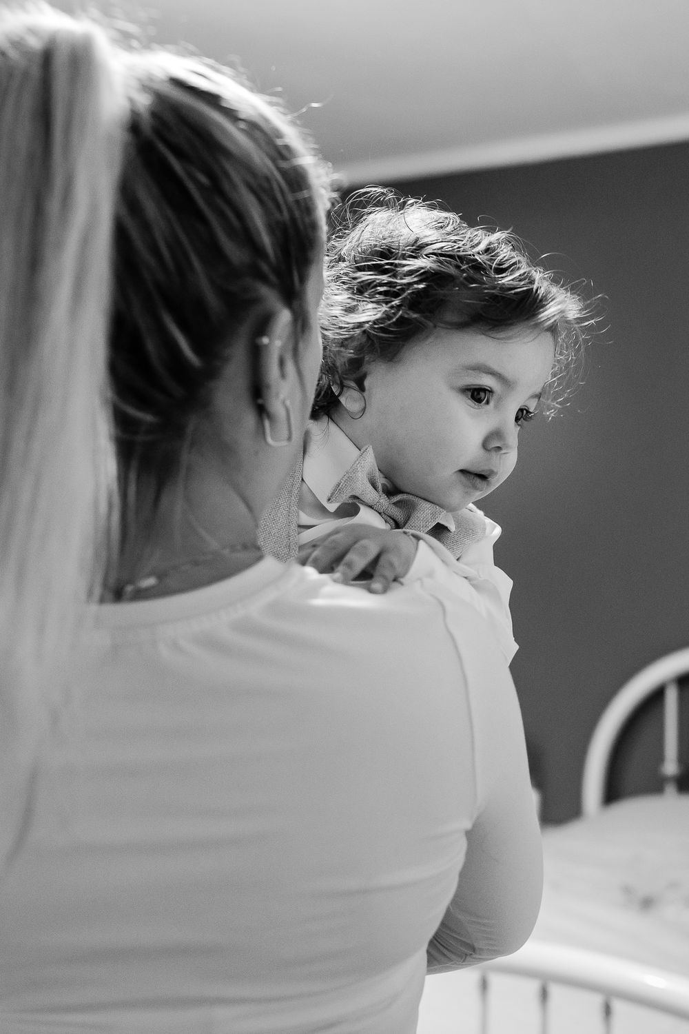 Black and white photo of a mother tenderly holding her toddler child in a cozy bedroom setting.