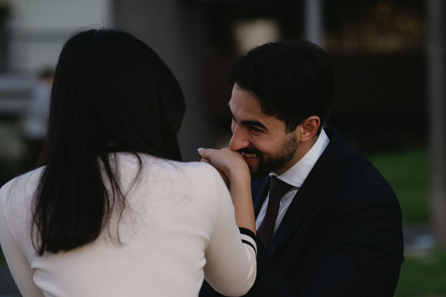 A romantic moment between a couple in formal attire as they share an intimate gesture outdoors at dusk.