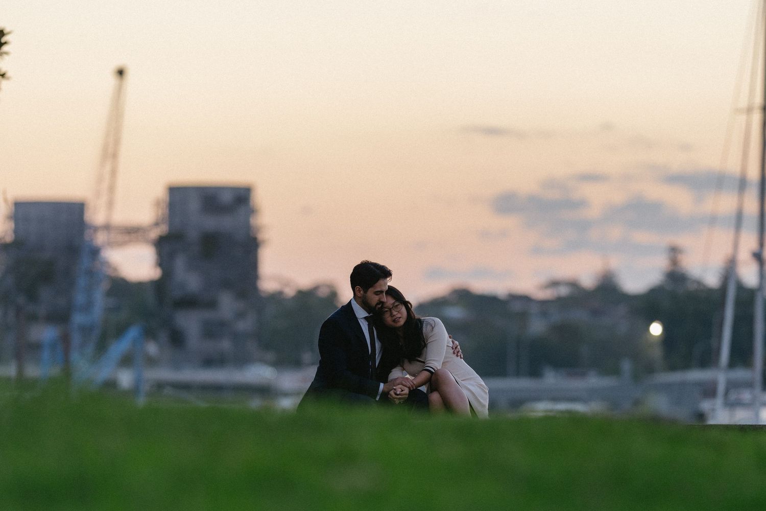 A couple embraces in silhouette against a sunset sky with city buildings in the background.