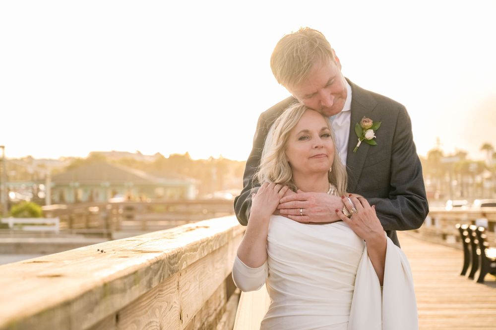Tender romantic moment between couple at golden hour on stone wall overlooking harbor.