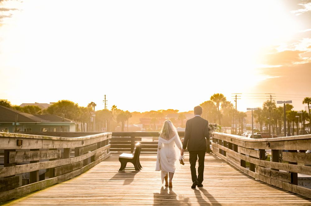 Couple walks on wooden boardwalk during golden sunset with their dog.