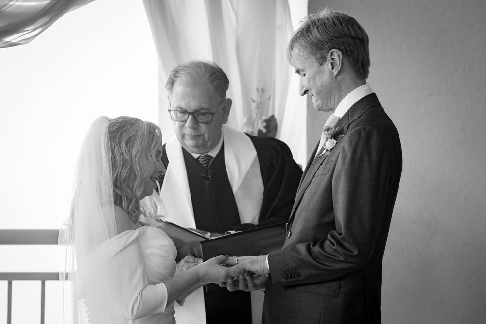 A traditional wedding ceremony taking place indoors with bride, groom and officiant in black and white.