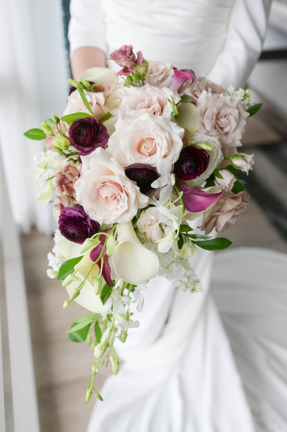 A stunning bridal bouquet with pink and burgundy roses cascading with greenery.