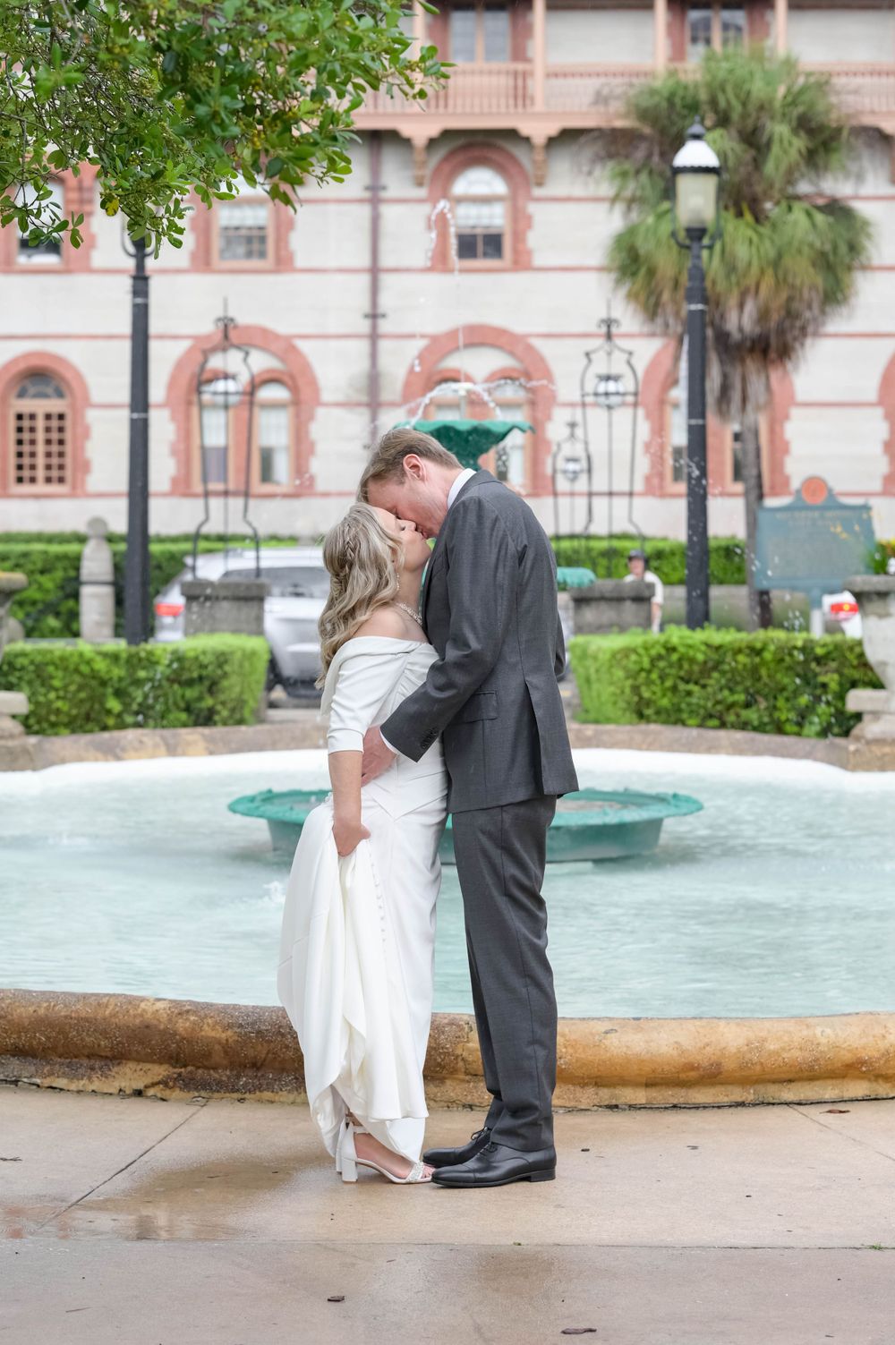 A romantic wedding moment by a fountain outside a historic pink building.