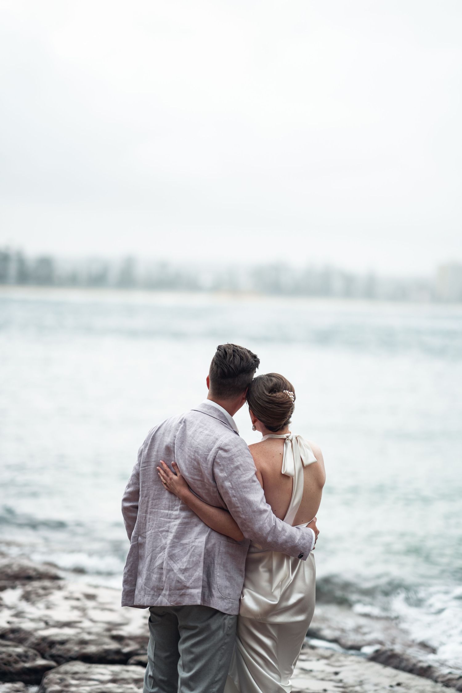 A couple shares an intimate moment while standing on rocky shores overlooking the ocean.