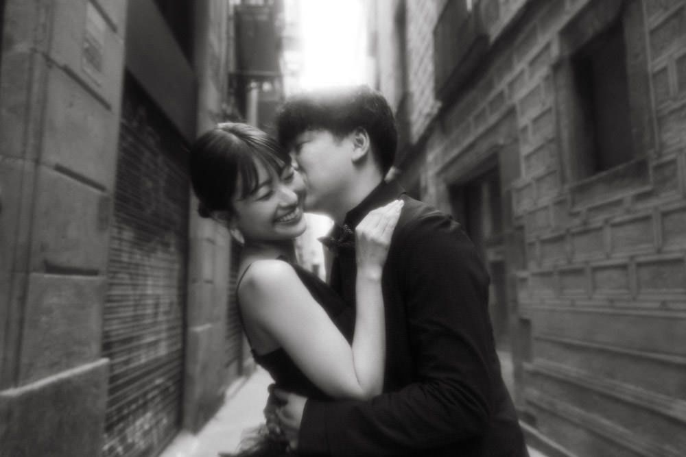 A romantic black and white portrait of a couple in formal wear embracing in an alley.