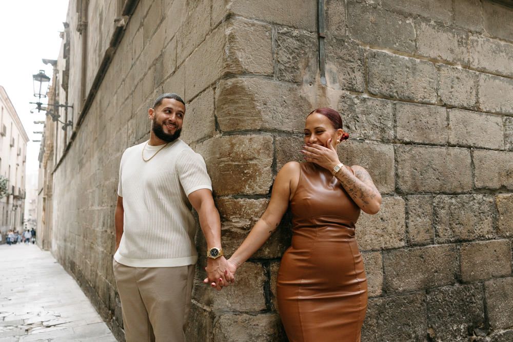 Couple posing against stone walls in an urban European setting.