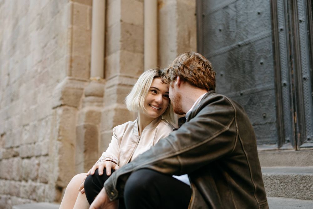 Couple embracing and laughing together against stone architectural backdrop.