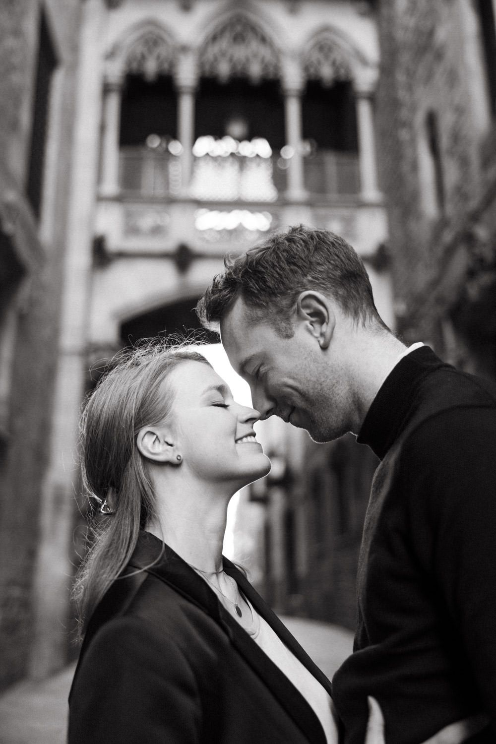 Romantic black and white portrait of couple sharing intimate moment in historic stone corridor.