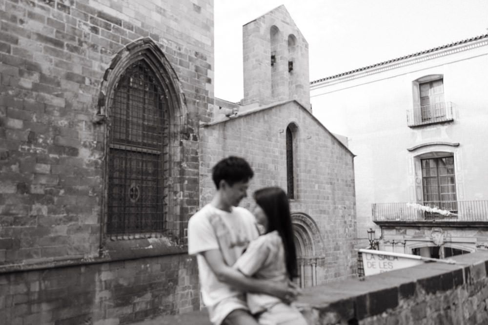 A couple shares an intimate moment against historic church architecture in black and white.