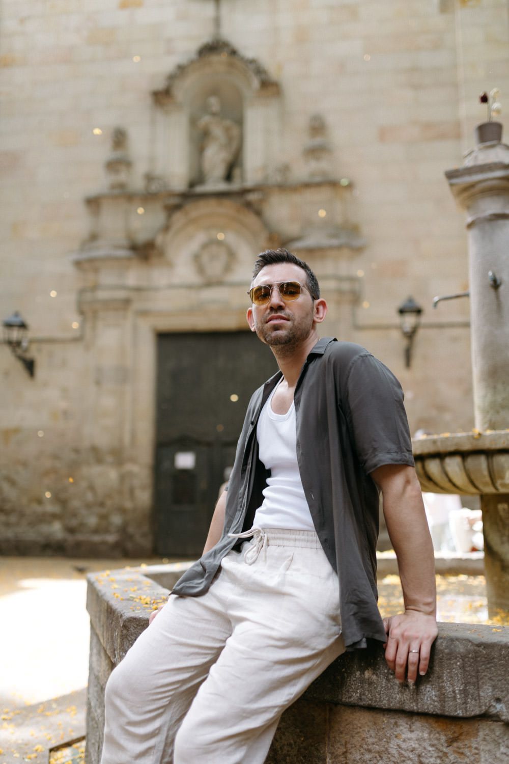 A casual traveler in sunglasses relaxes on stone wall near historic church architecture.