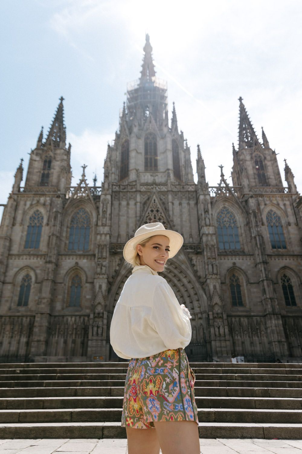 A person in summer attire poses on cathedral steps with Gothic architecture in the background.