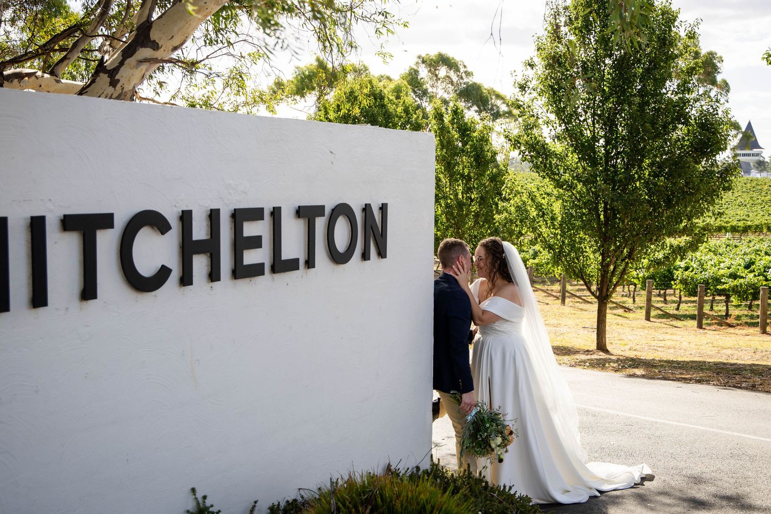 Outdoor wedding ceremony setup with wooden chairs and floral arrangements on a gravel surface.