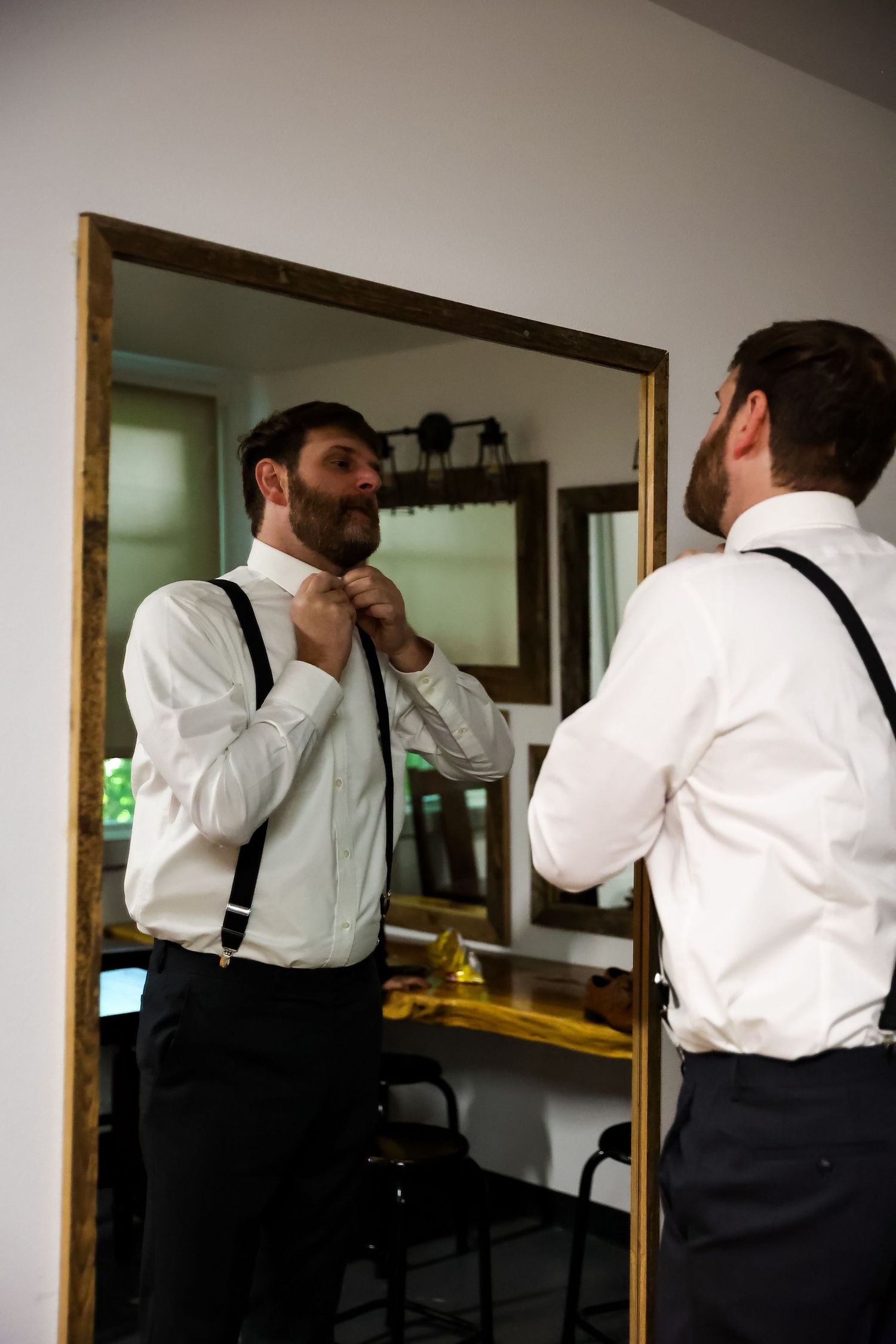 A mirror reflection shows someone adjusting a tie while wearing formal attire.