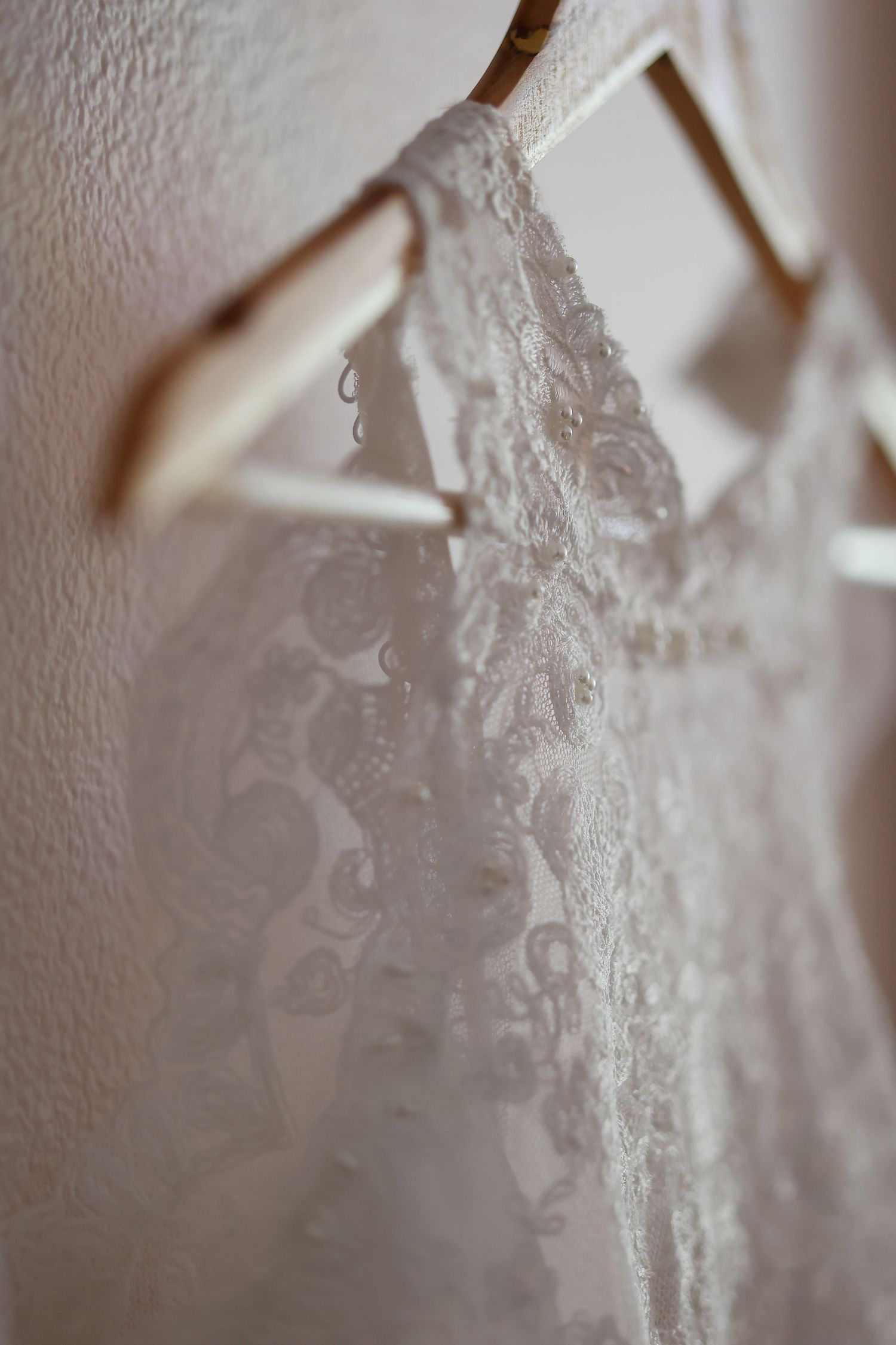 Close-up detail of delicate white lace on a wedding dress hanging against a light wall.