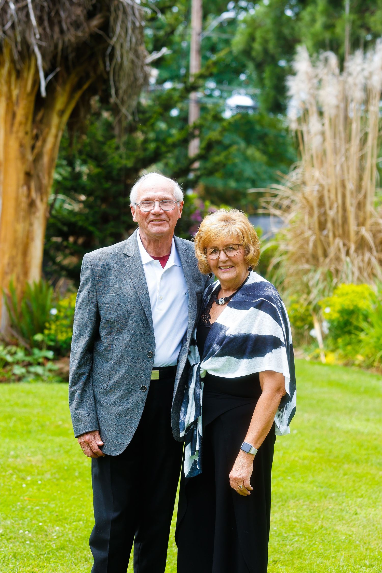 A couple poses outdoors in formal attire against a backdrop of ornamental grasses.