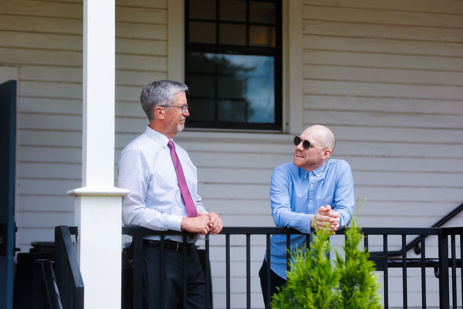 Two men having a conversation on a white porch with columns.