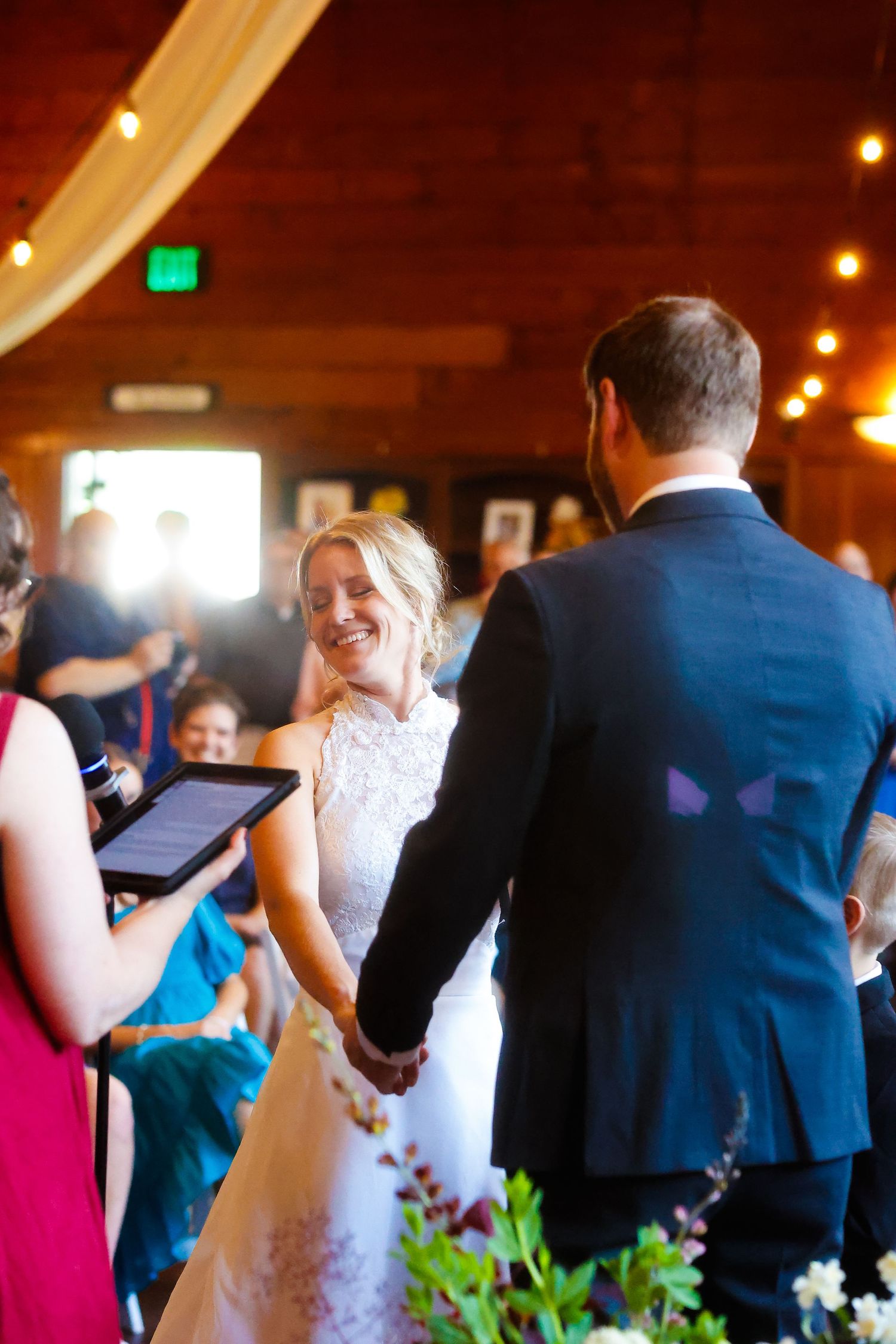 Wedding ceremony in rustic venue with wooden beams and string lights overhead.