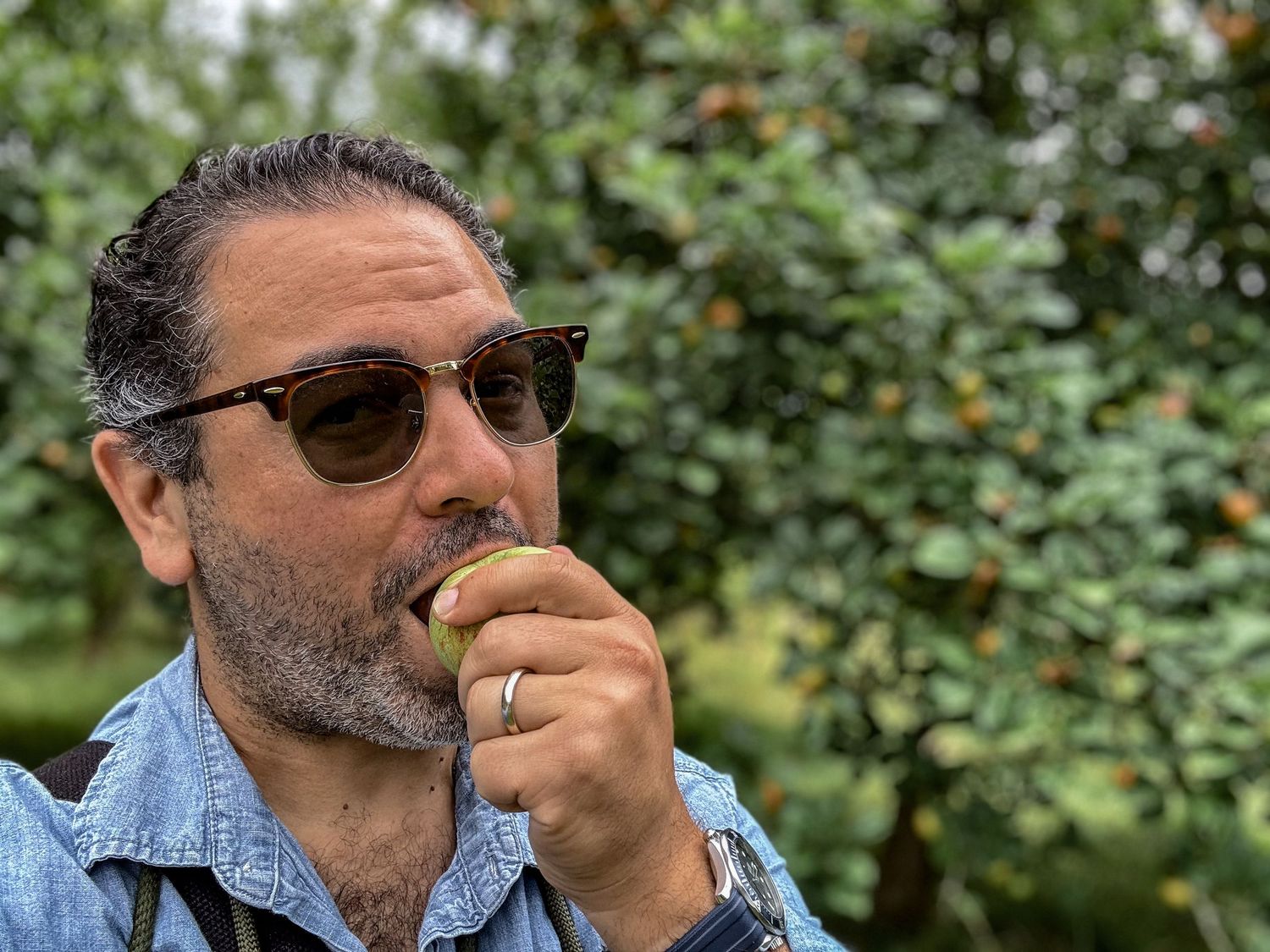 A casual outdoor portrait of someone eating while wearing sunglasses and denim.