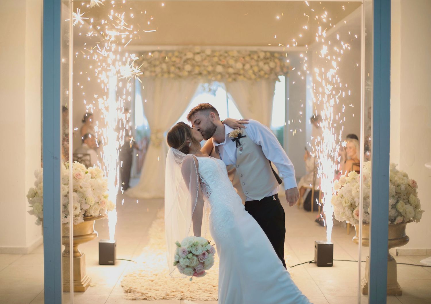Married couple kissing while fireworks are behind them.
