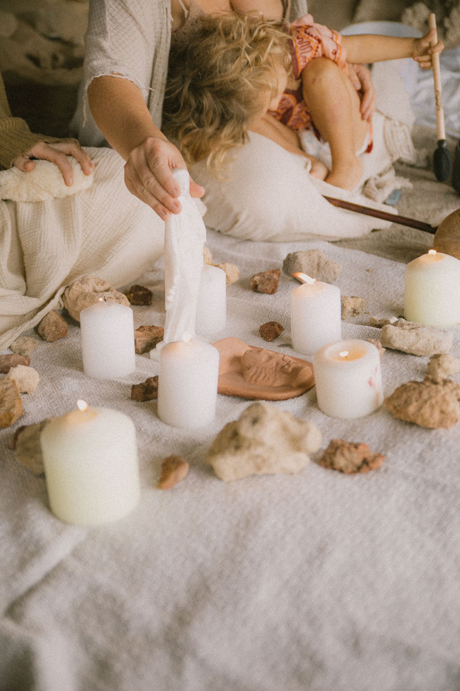 Hands arranging white pillar candles on a textured white cloth surface.