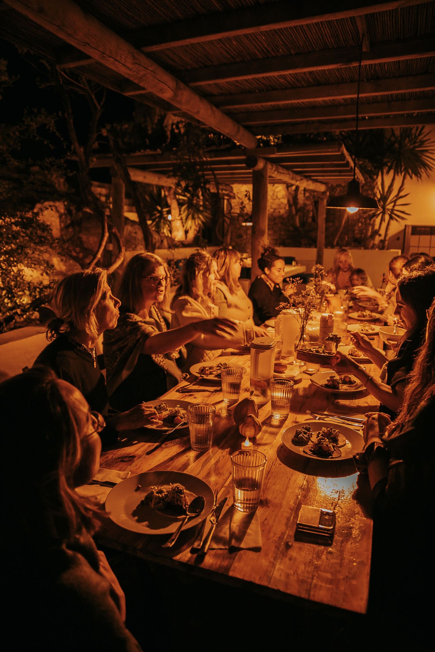 Dimly lit dinner gathering with people seated at a rustic wooden table.