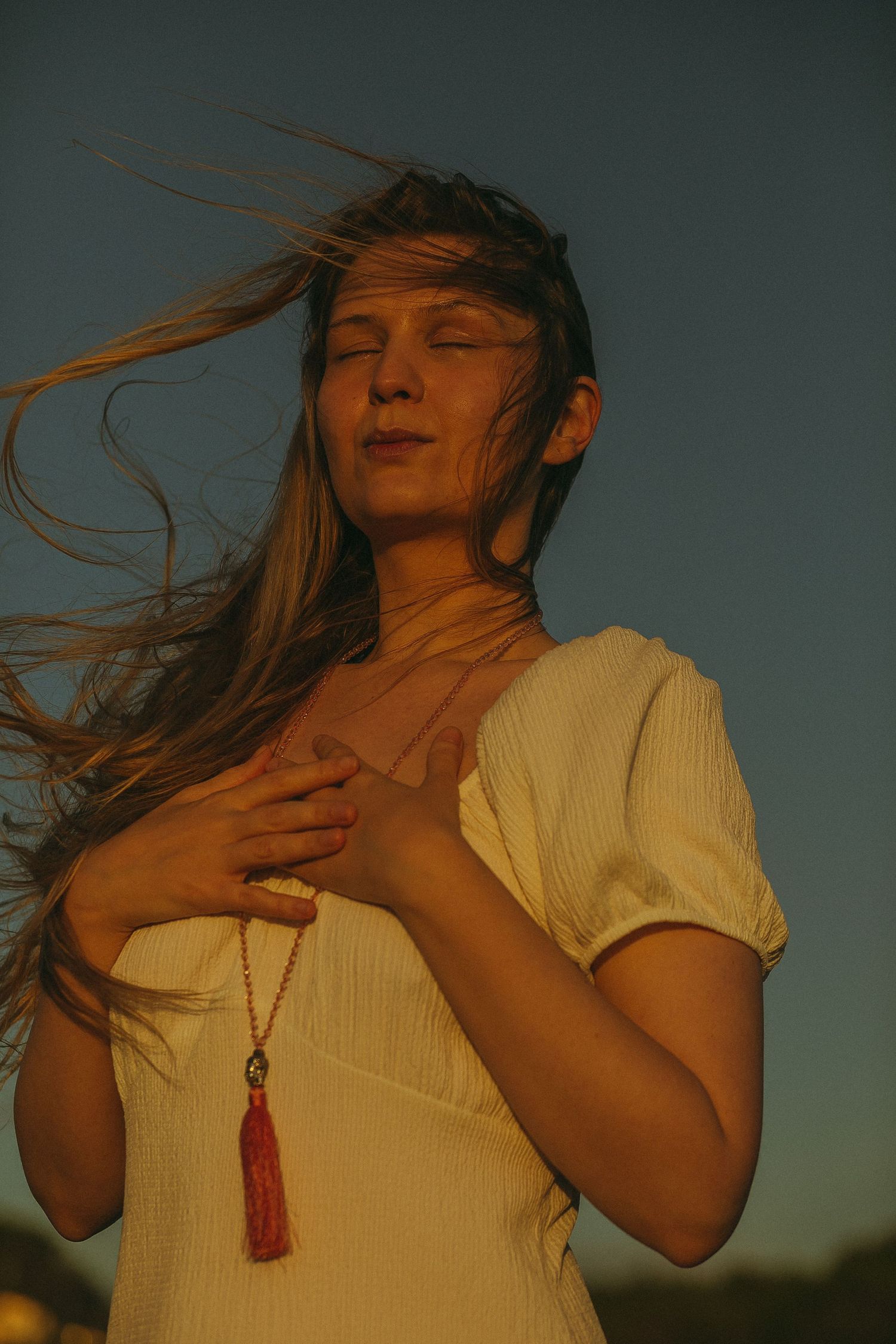 Person in white top with red necklace dancing in golden sunset light with hair flowing.