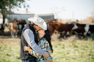 A tender moment shared in front of cattle with southwestern style fashion and a cowboy hat.