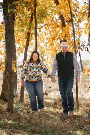 A couple walks hand in hand under golden autumn trees wearing matching southwestern style sweaters.