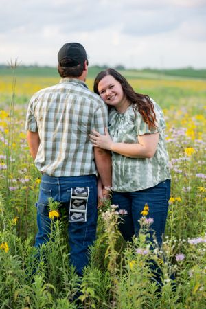 Couple stands in wildflower field with ultrasound photos displayed on back pocket.