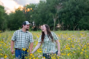 Couple shares genuine laughter while standing among yellow wildflowers at sunset.
