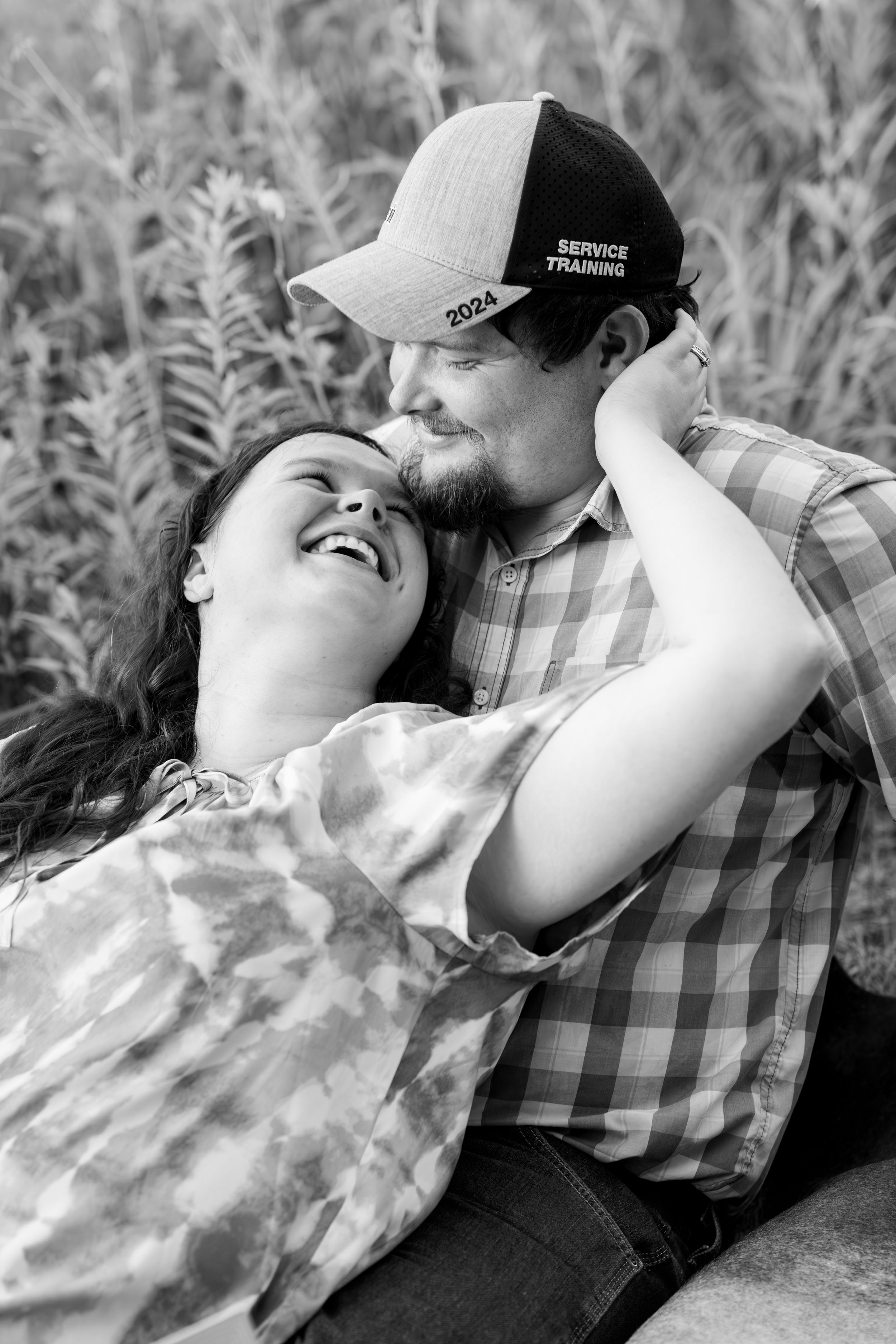 Black and white portrait of couple sharing intimate moment in tall grass.