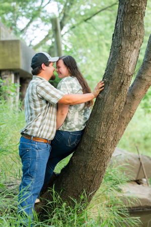Couple shares intimate moment leaning against tree trunk by stream.