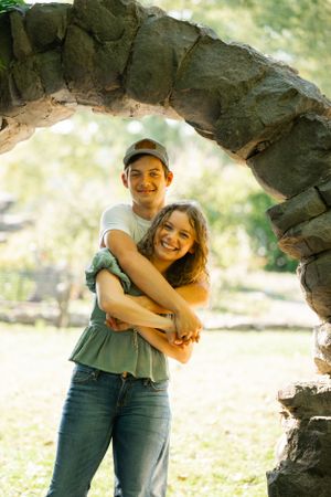 A joyful embrace under a rustic stone archway in a park setting.