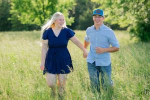 A couple walks hand in hand through a sunny summer meadow with bright green foliage.