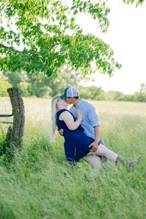 A romantic moment between two people in a sunlit field under a tree.
