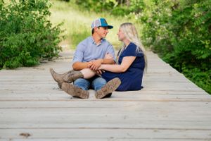 A couple sitting close together on a wooden boardwalk path surrounded by green foliage.