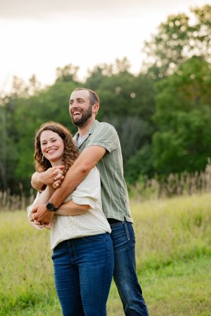 Happy couple embraces while laughing together in a sunlit grassy field at sunset.