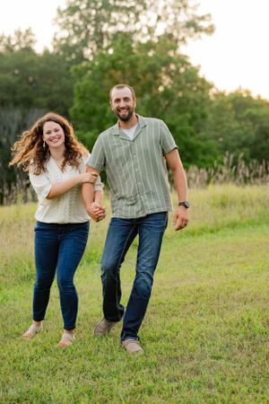 Joyful couple running and laughing together in a natural meadow setting.