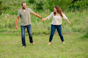 Playful couple holds hands while dancing in a green summer field.
