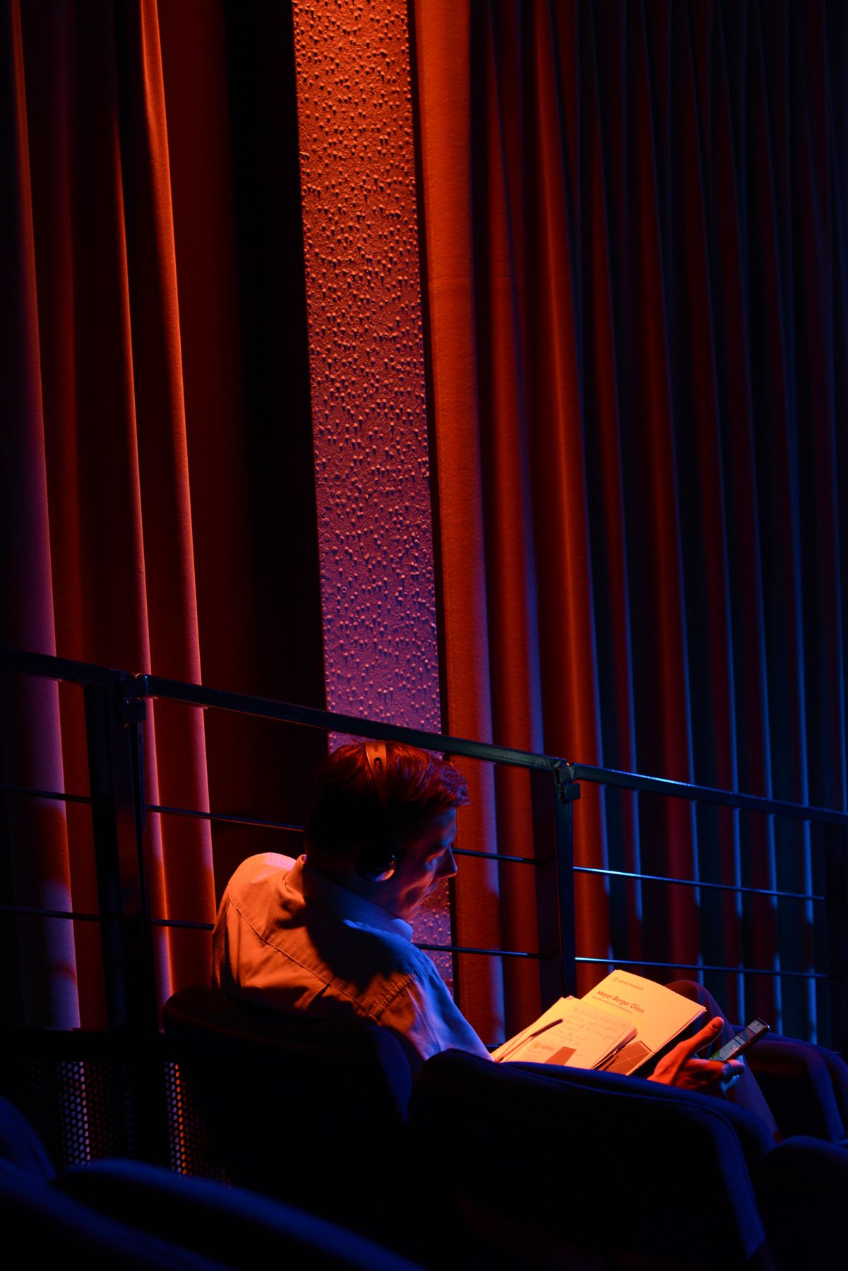 Red theater curtains illuminated by dramatic stage lighting in dark auditorium.