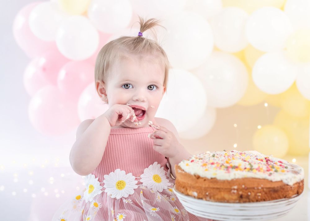 A pink dress with daisy details and a birthday cake creates a dreamy first birthday scene with soft bokeh background.