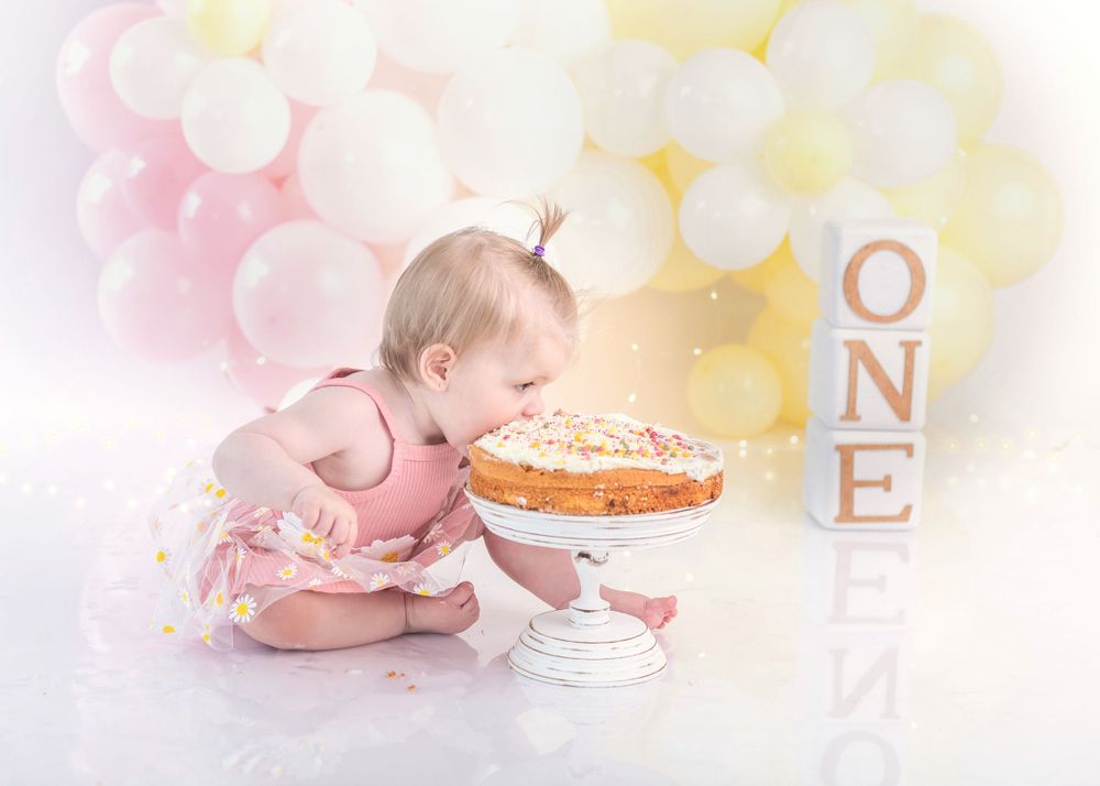 Whimsical cake smash scene with pink and yellow balloons and ONE letter blocks in the background.