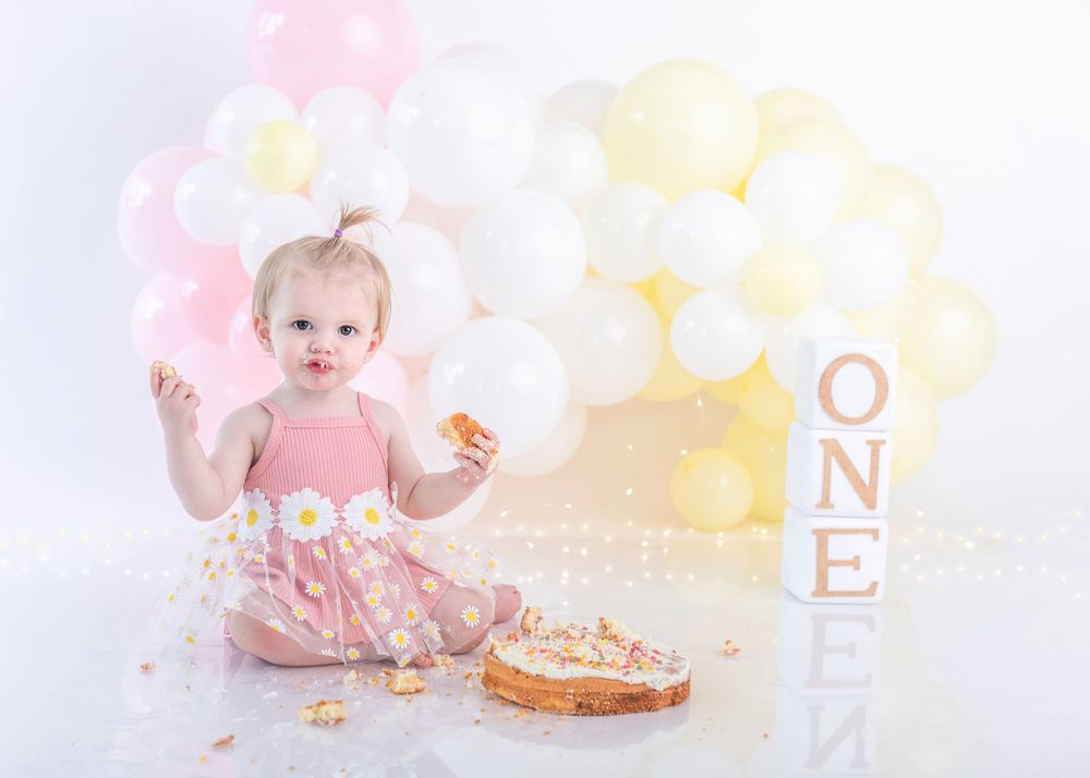 First birthday celebration scene with cake crumbs and ONE blocks against pink and yellow balloons.