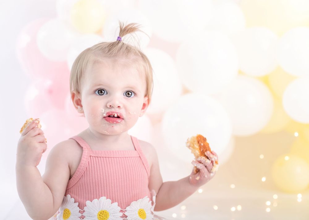 Festive first birthday scene with pink ribbed top and daisy details against soft bokeh background.