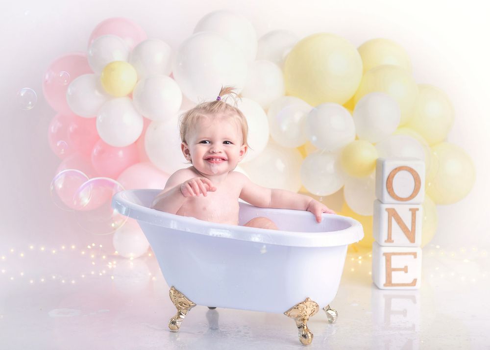 Vintage-style miniature bathtub photo setup with pink and yellow balloon backdrop.
