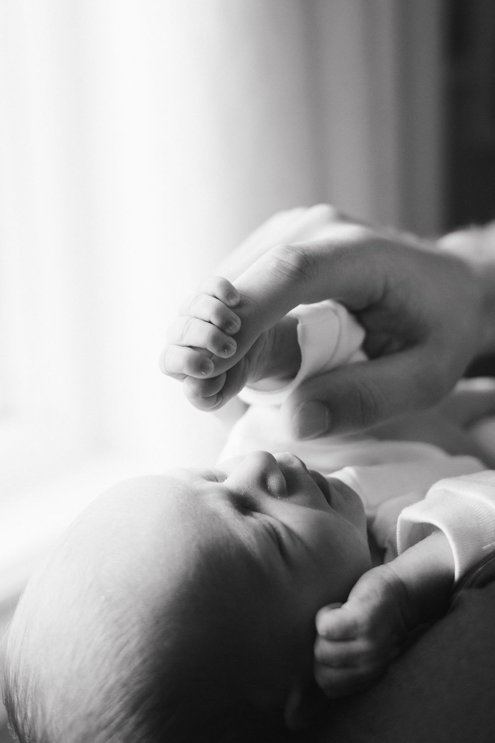 Black and white close-up photograph of a sleeping baby's face and tiny hand being gently touched.