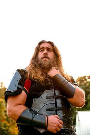 Cosplayer wearing medieval armor and leather gear poses dramatically at golden hour.